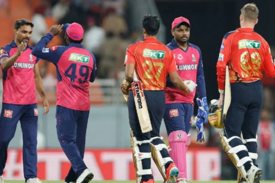 Cricket players in pink jerseys celebrate on the field, high-fiving as two wear pads and carry bats after a wicket. A stadium backdrop with spectators visible in the stands.